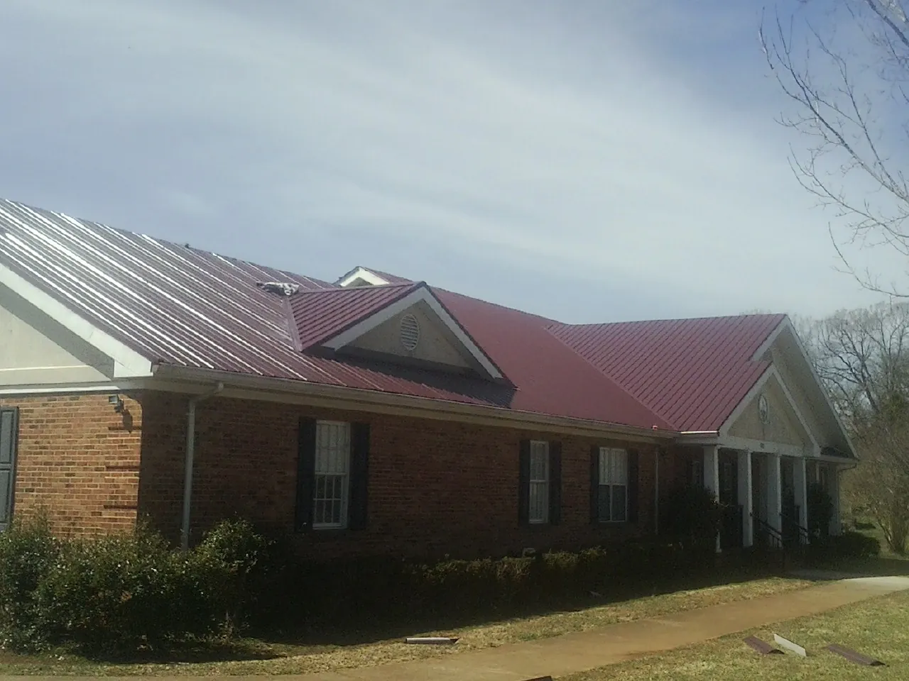 Red metal roof with gabled entries on a long brick building, from a Hail Damage Roof Repair job in Dillsburg