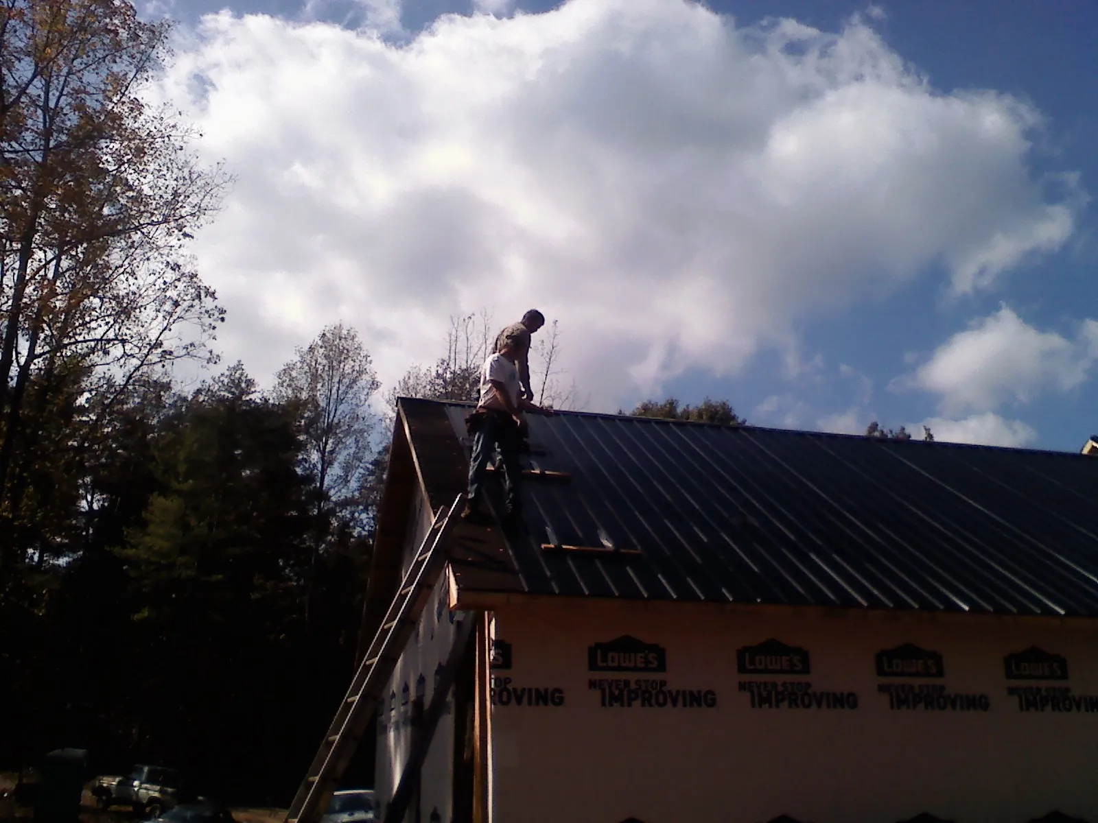 Roofer fastening dark metal panels high against a cloudy sky, from a Roof Inspection job in Dillsburg