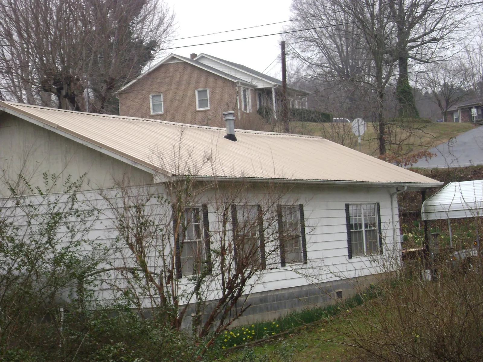 Tan metal roof on a white sided house set into a hillside — Commercial Roofing by Roofing Brothers in Dillsburg